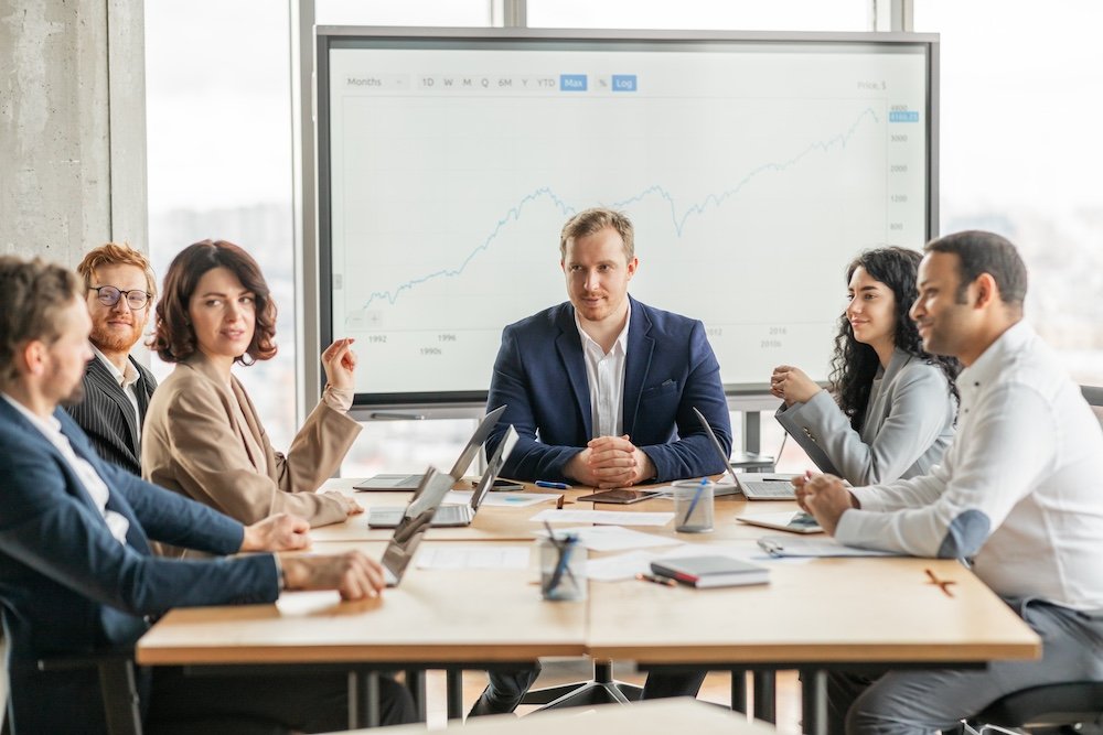 Business team meeting discussing growth chart presentation in modern office with professionals collaborating around table